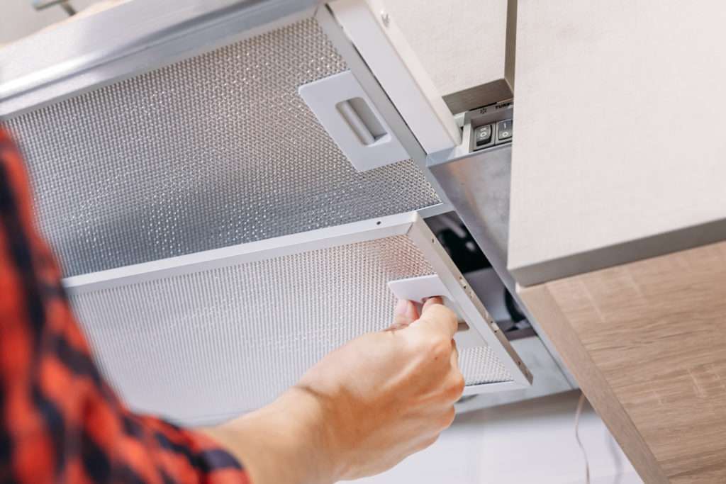 Man repairs hood in kitchen. Replacement filter in cooker hood