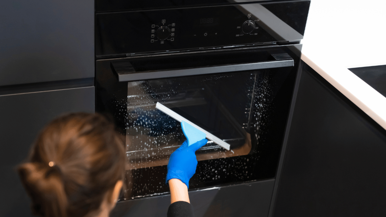A woman using a rag to clean both inside and outside of the oven.