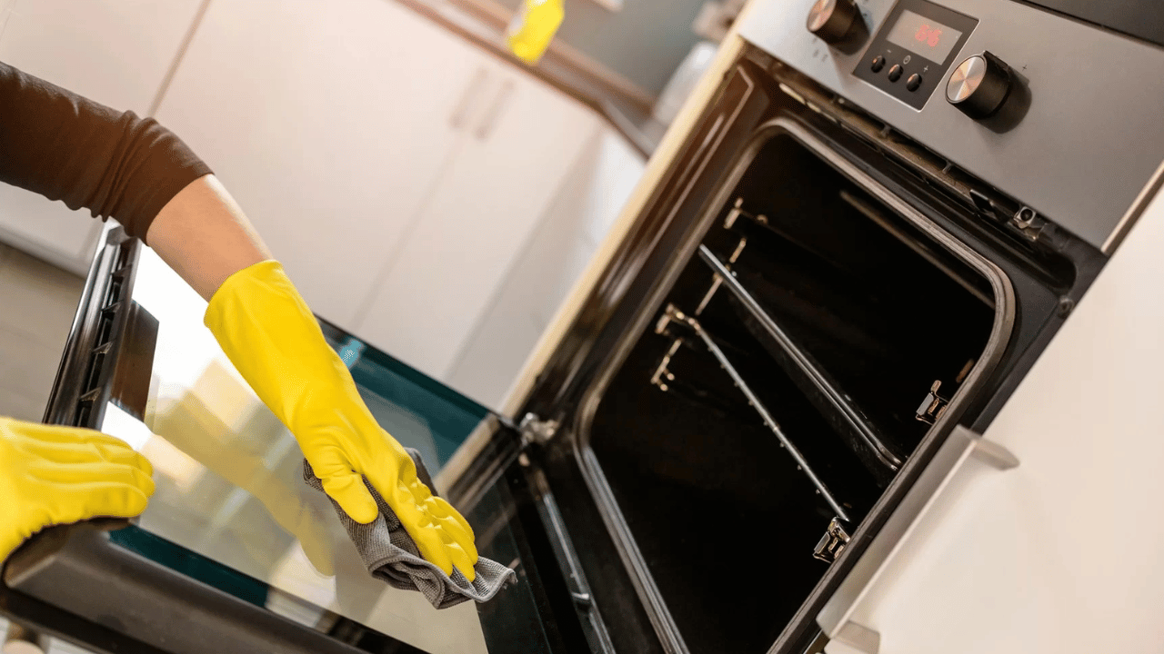 A woman using a rag to clean both inside and outside of the oven.