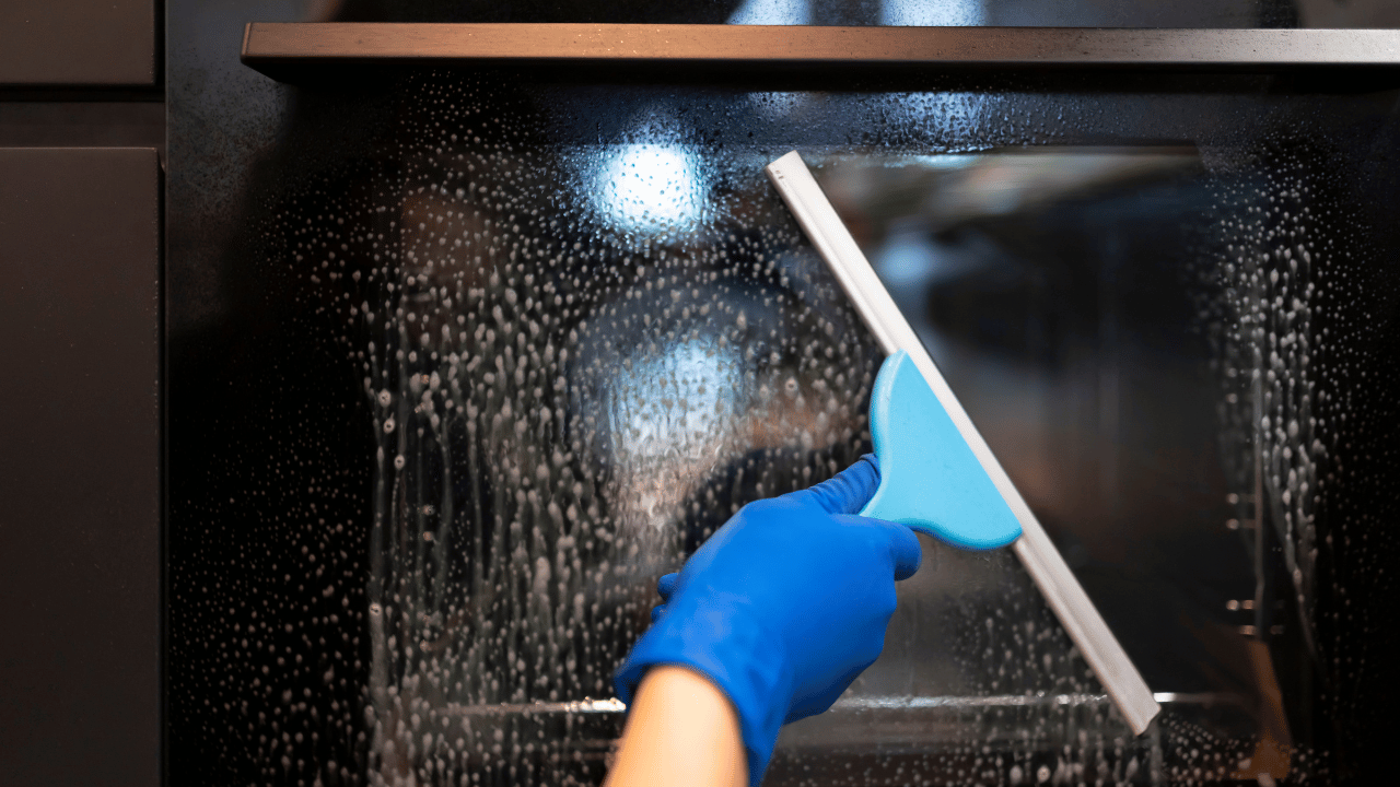 A woman using a rag to clean both inside and outside of the oven.