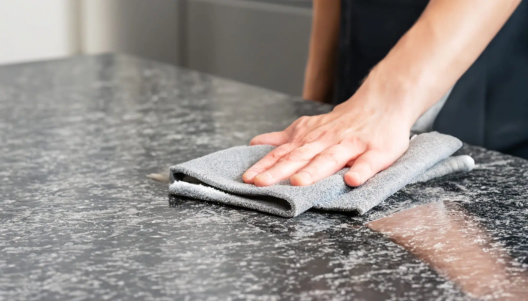 A-person-cleans-a-granite-countertop-following-Hilltop-Surfaces-granite-maintenance-tips